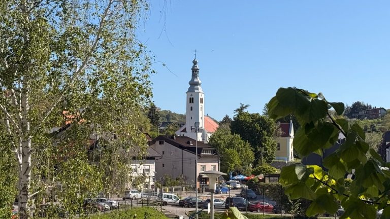 View of Samobor with its historic church tower under a clear blue sky, surrounded by greenery.
